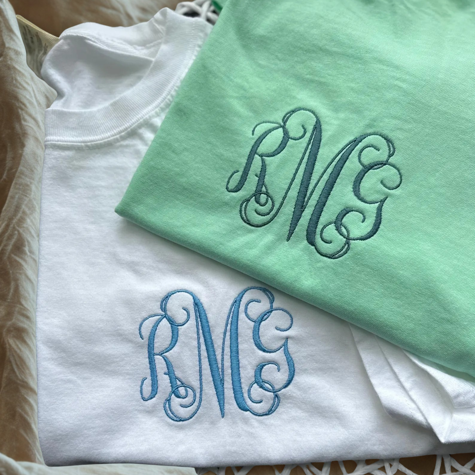 Two folded shirts with monogrammed initials on a textured surface
