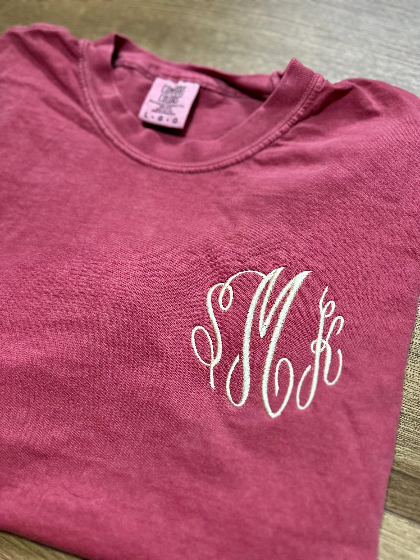 Maroon t-shirt with a white monogram on a wooden surface