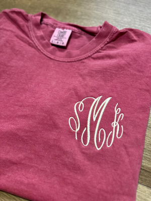 Maroon t-shirt with a white monogram on a wooden surface