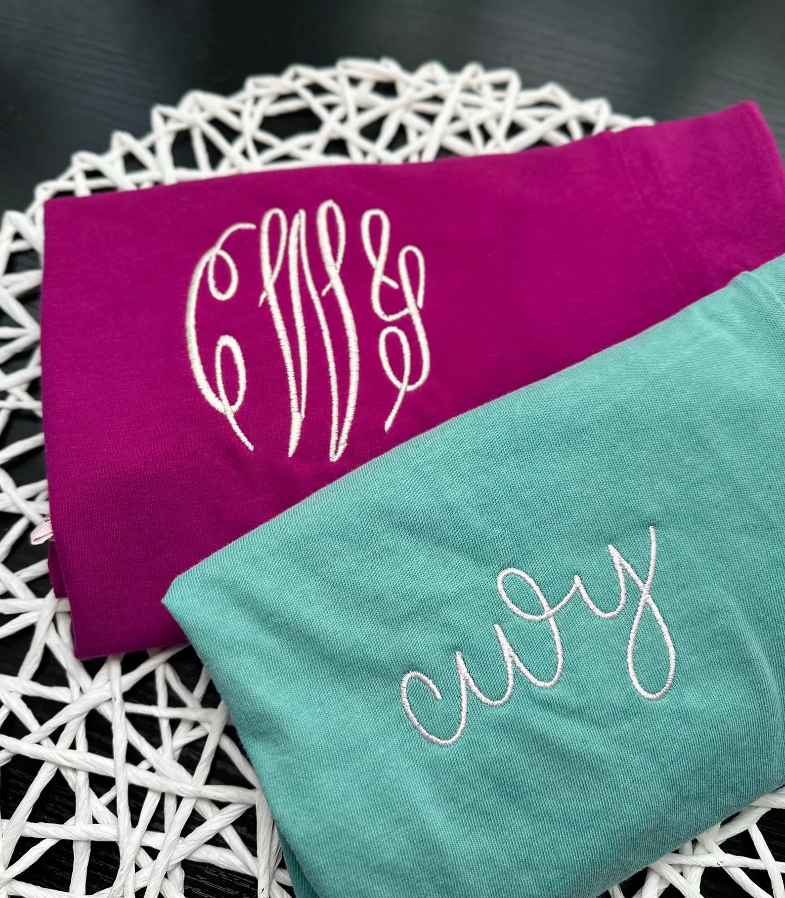 Two towels, one purple and one green, with embroidered monograms on a white doily.