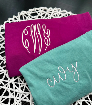 Two towels, one purple and one green, with embroidered monograms on a white doily.