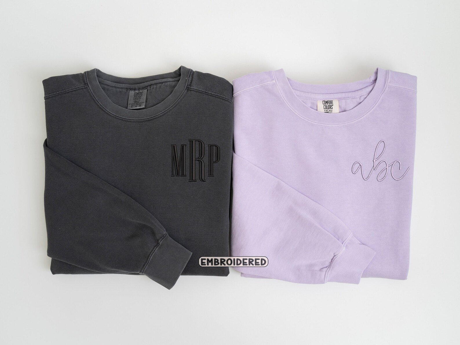 Folded black sweatshirt with 'MRP' and lavender sweatshirt with 'abc' on a white background